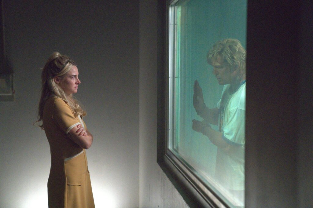 Shailene Woodley watches through the glass as Ritchson presses his hand against it in "Motor City." - The Latino Slant