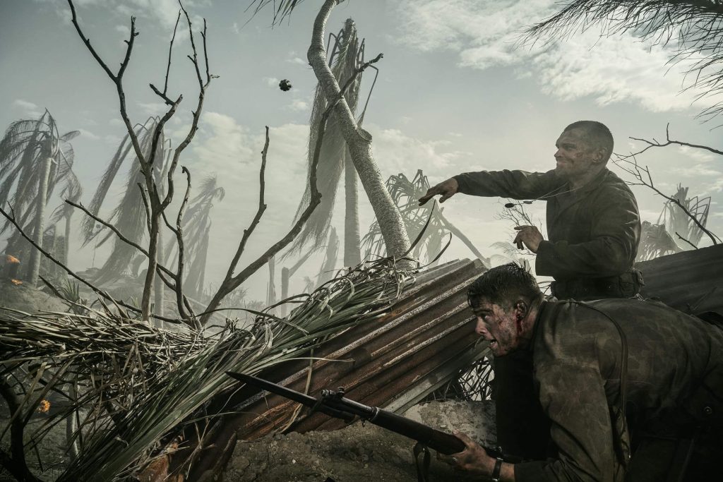 Ray Nicholson as Tony Butkovich hurls a grenade as Nicholas Galitzine as John McLaughry braces amid shattered palms in “The Mosquito Bowl.” - The Latino Slant